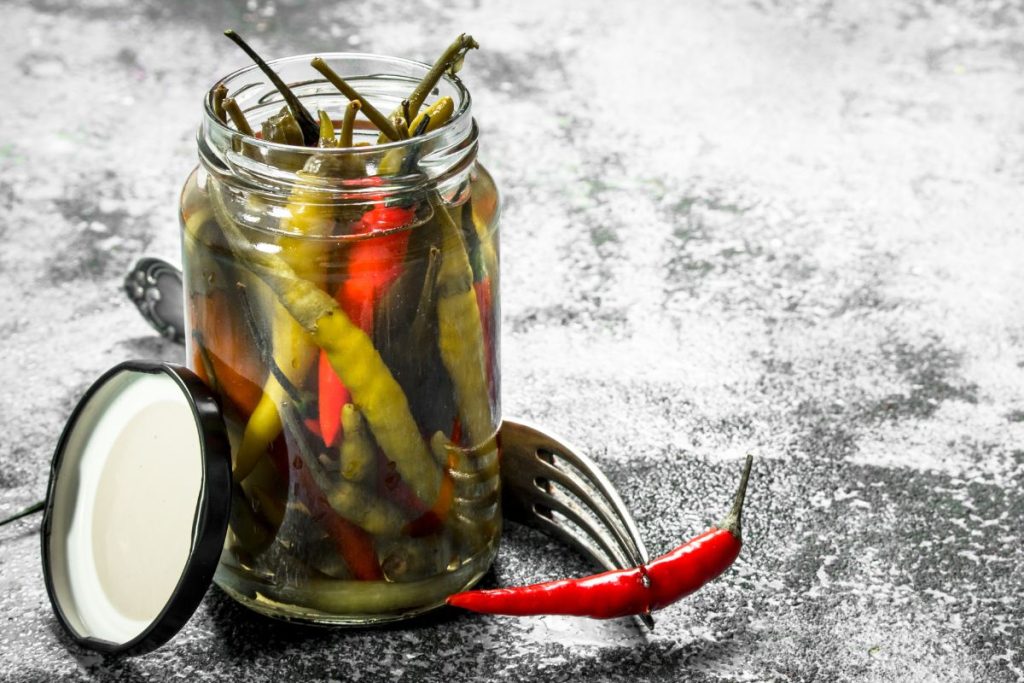 Red yellow and green hot pickled peppers in open canning jar