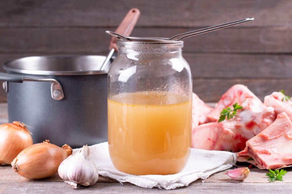 Jar with strainer on the top surrounded by meat bones and shallots