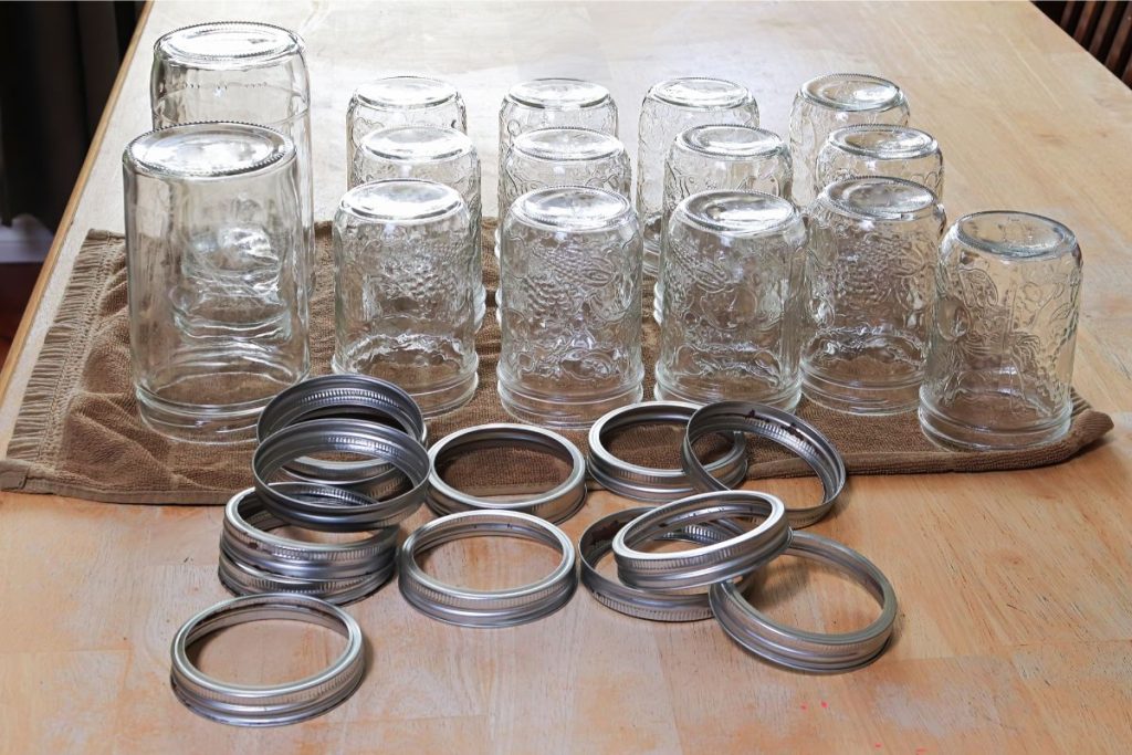 Canning jars upside down on a towel with a pile of screw bands in front of them