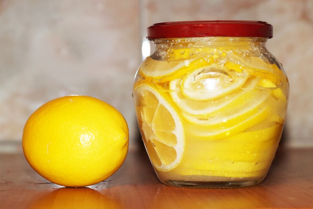 Jar of sliced lemons in jar next to a whole lemon