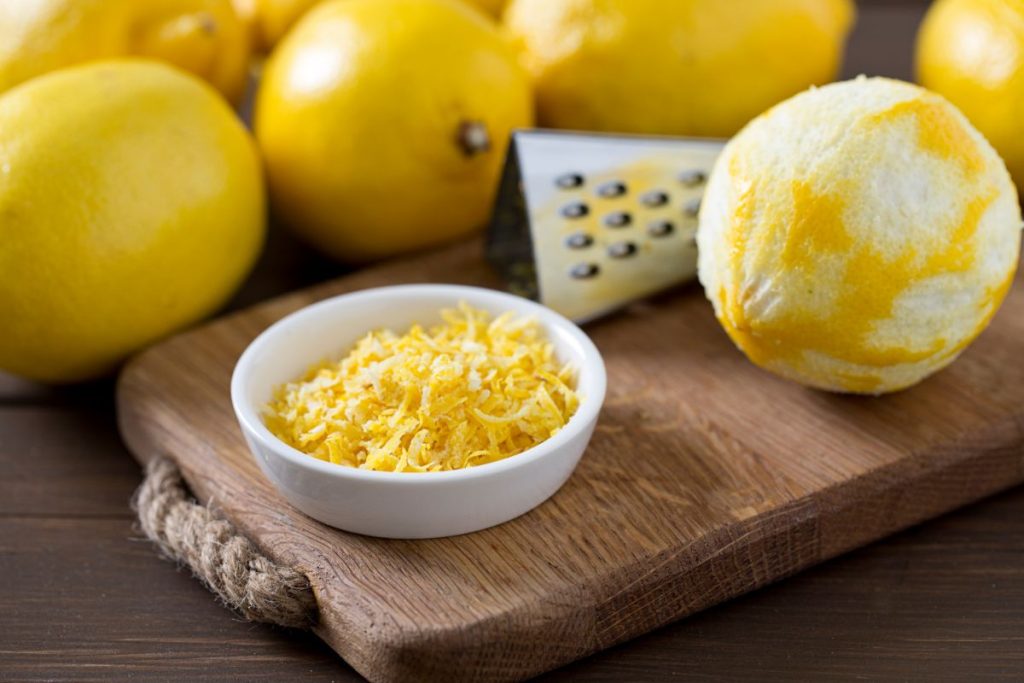 Container with lemon zest next to freshly zested lemons