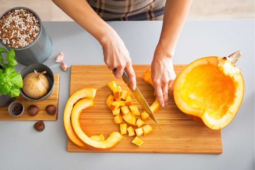 Woman dicing pumpkin into one inch pieces from two inch strips of pumpkin.