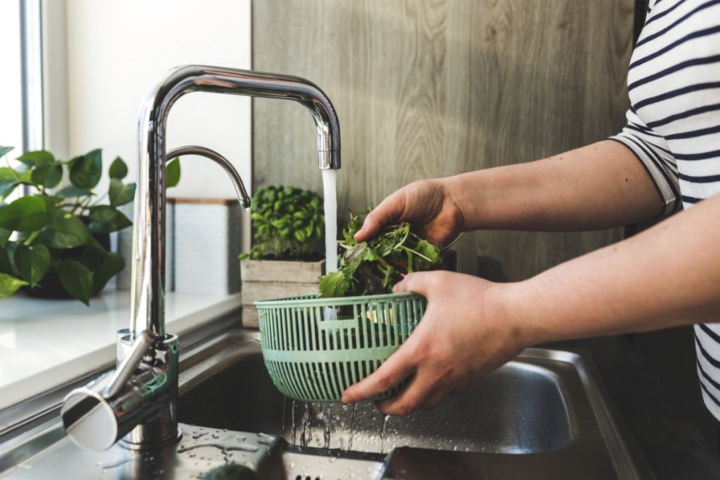 Rinsing mustard greens in running water at sink