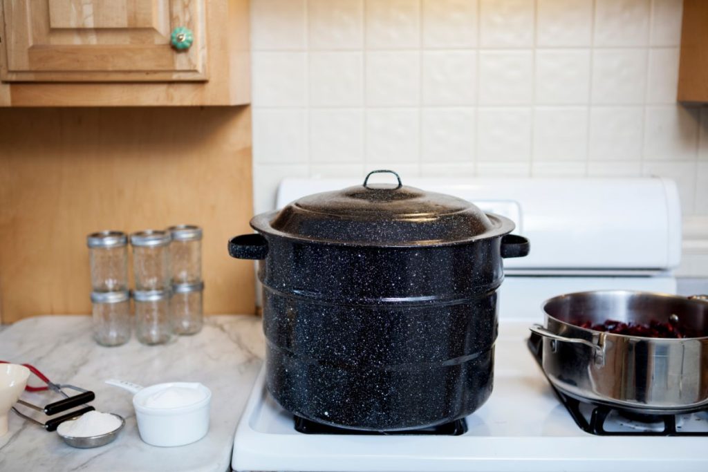 boiling water canner and pot on stovetop with canning supplies on countertop