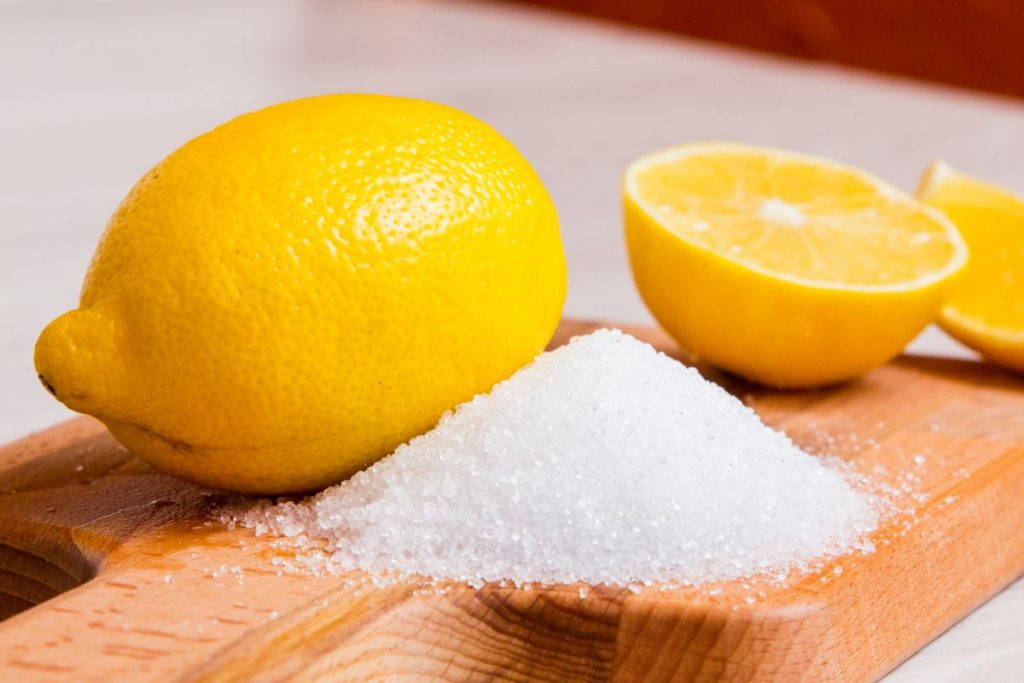 Powdered citric acid next to fresh lemons on cutting board