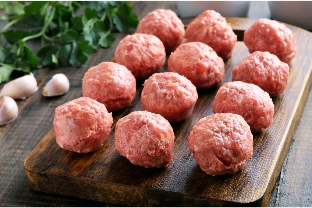 Cutting board with several rows of raw meatballs that are between 3 and 4 inches wide