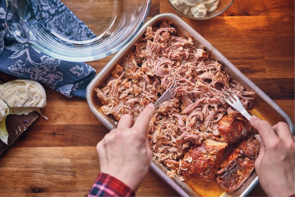 Man using two forks to separate pulled pork meat into shreds