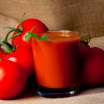 glass of tomato juice surrounded by fresh tomatoes