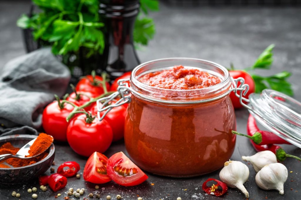 Jar of tomato sauce surrounded by tomato sauce ingredients