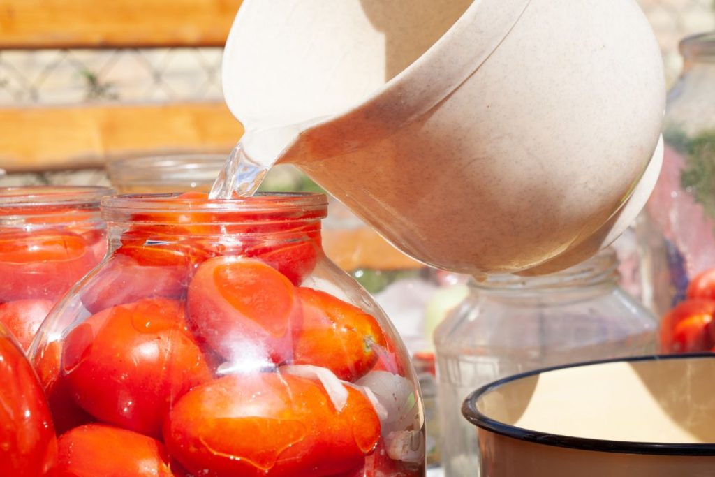 Water being poured into a jar of fresh tomatoes