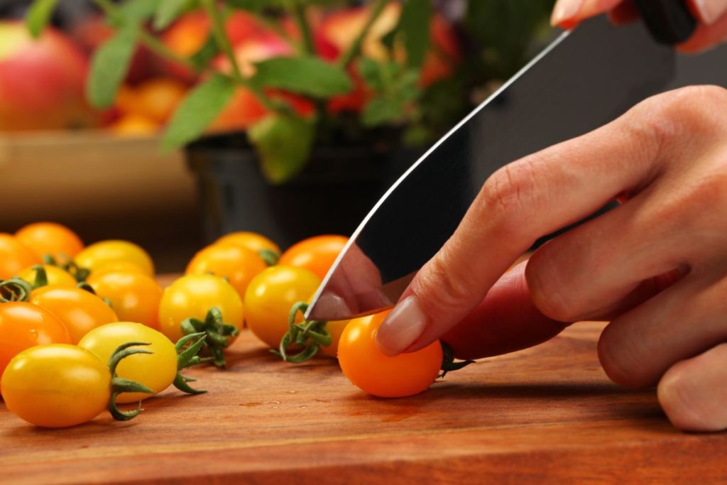 Cutting yellow tomatoes in half on a cutting board