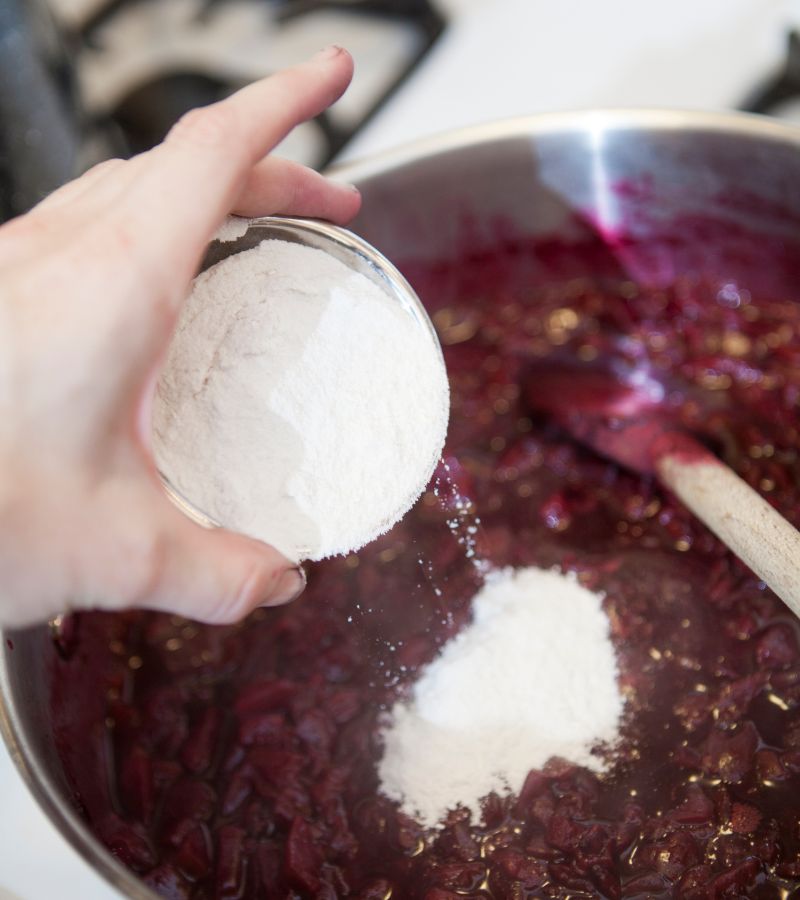 Woman adding powdered pectin to a jam mixture