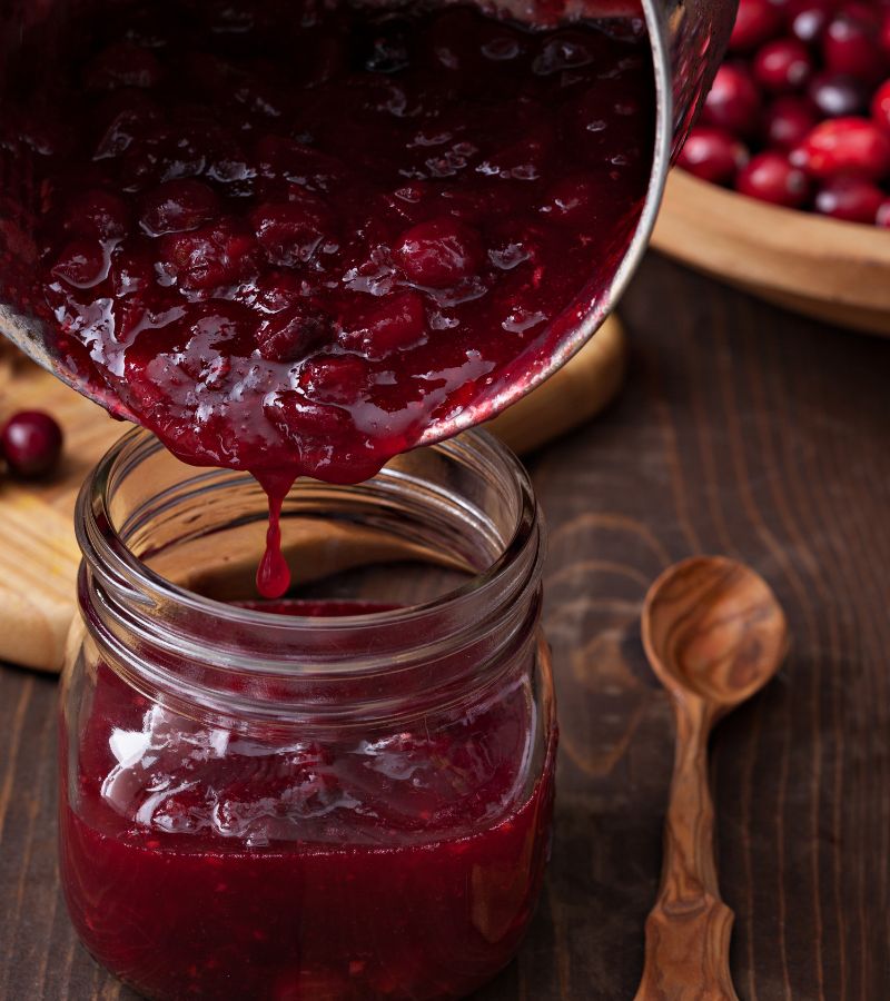 Canning cranberry sauce by pouring cranberries into a canning jar