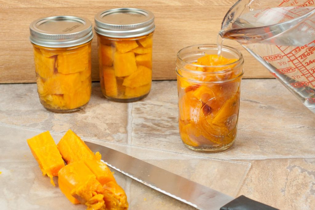 Canned sweet potatoes being topped with water in canning jars