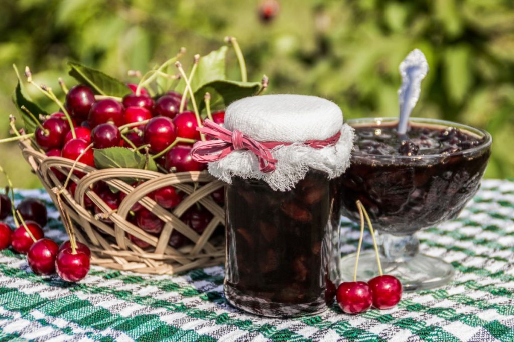 Cherry jam in a jar with a bowl of jam on a picnic table