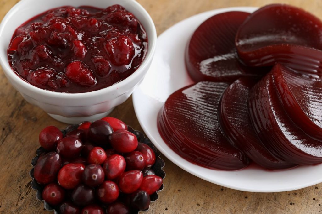 Jellied cranberry slices next to bowl of whole berry cranberry sauce