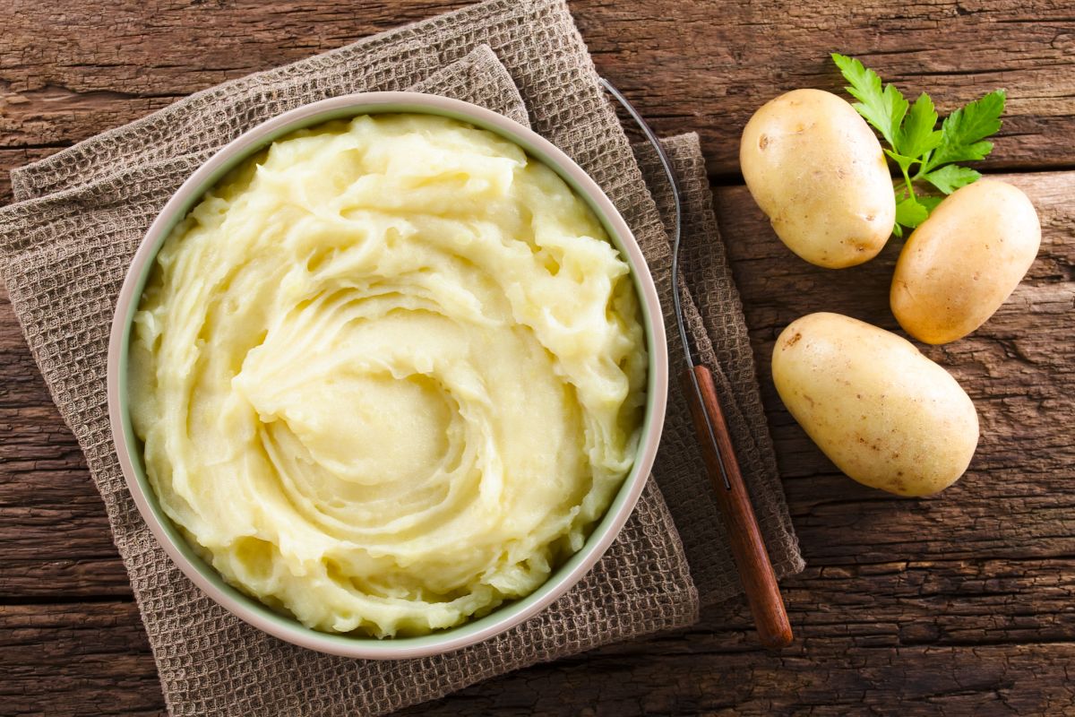 Mashed potatoes in a bowl next to fresh potatoes