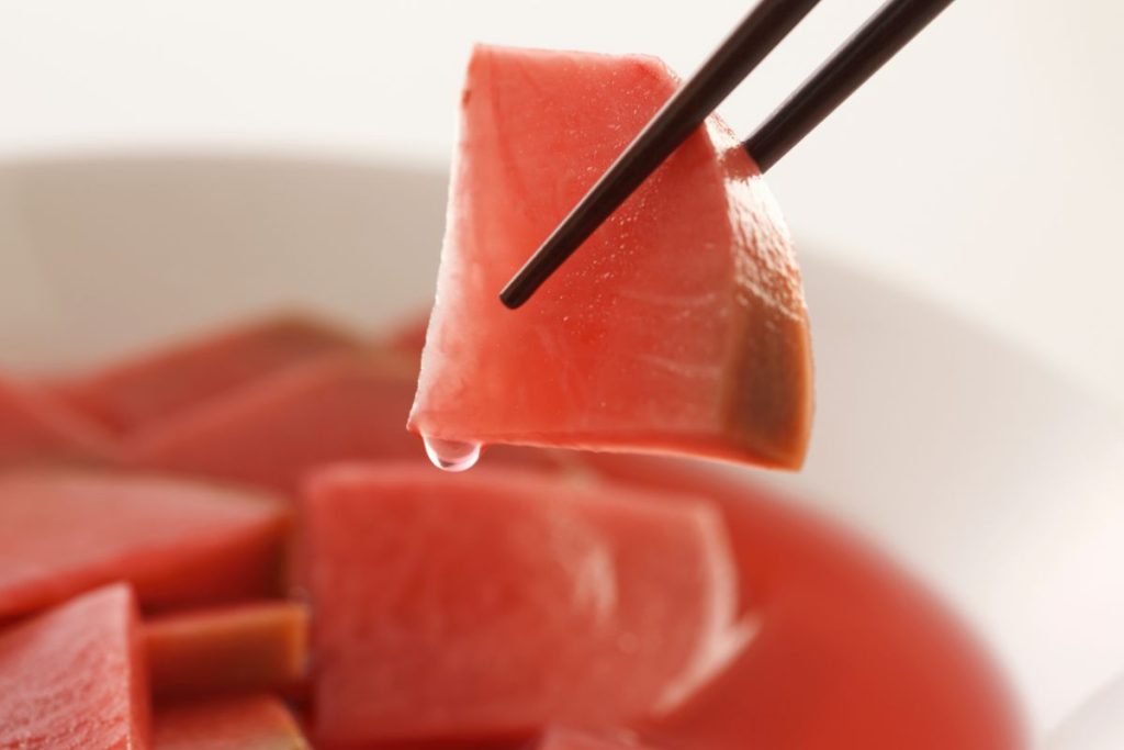 A piece of pickled radish held by chopsticks