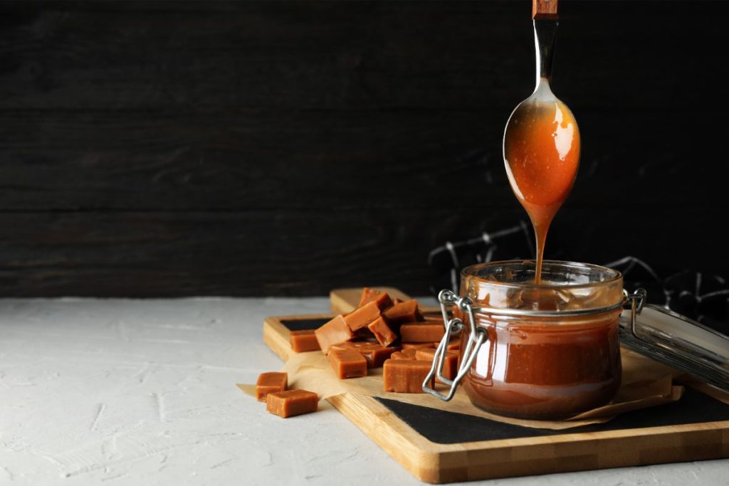 Dark colored caramel sauce spoon being lifted out of jar
