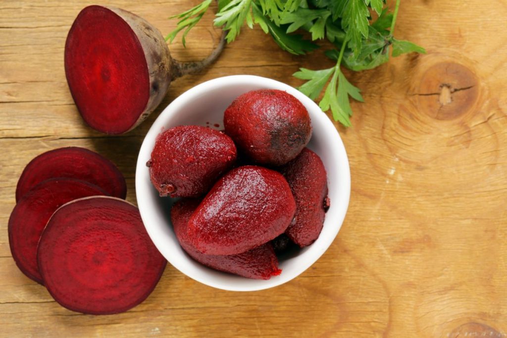 Bowl of boiled and peeled beets next to sliced fresh beets.