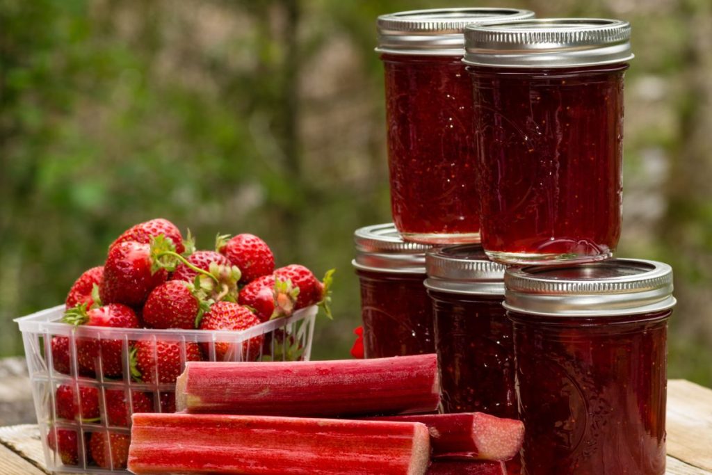 Strawberries, rhubarb stalks and jars of strawberry rhubarb jam on a picnic table