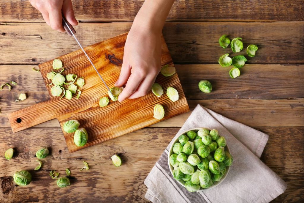 Woman slicing Brussels sprouts in half on cutting board