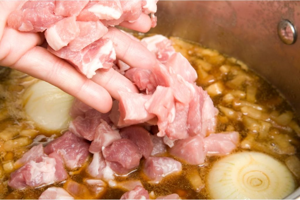 Woman adding raw pork to a soup mixture