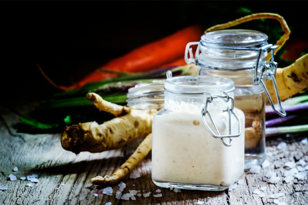 Jar of pickled horseradish next to horseradish roots