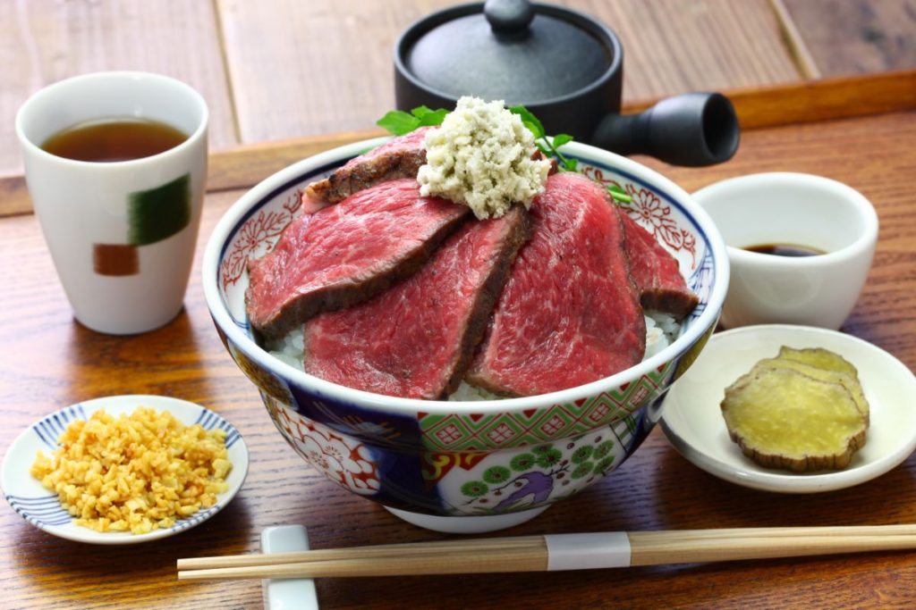 Bowl of A5 Wagyu beef topped with horseradish sauce next to small plates of pickled vegetables