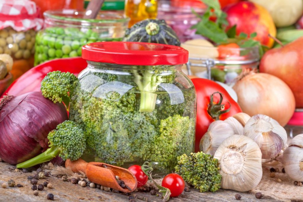 Jar of broccoli pickles surrounded by fresh vegetables