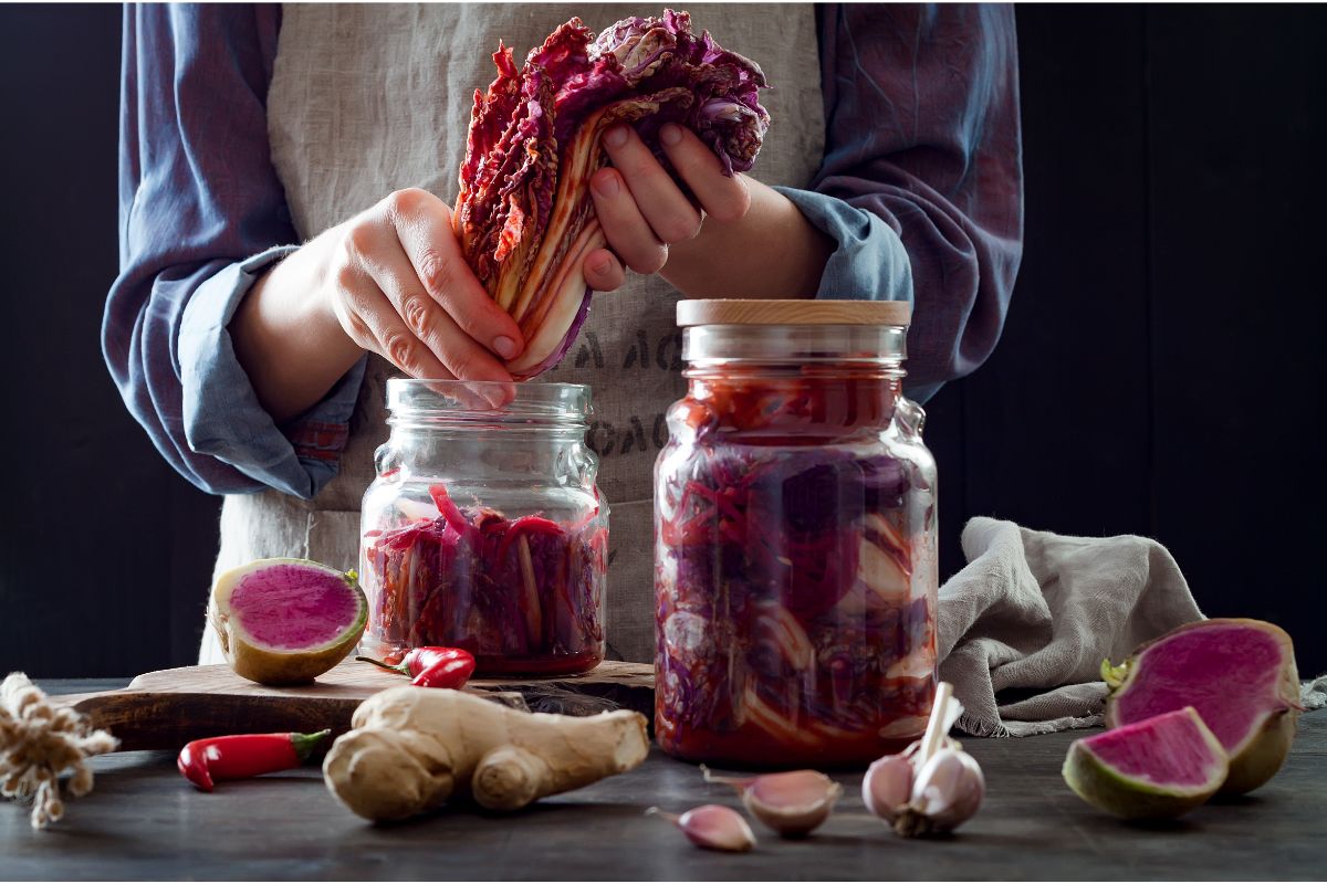 Woman canning kimchi and filling glass jars with cabbage