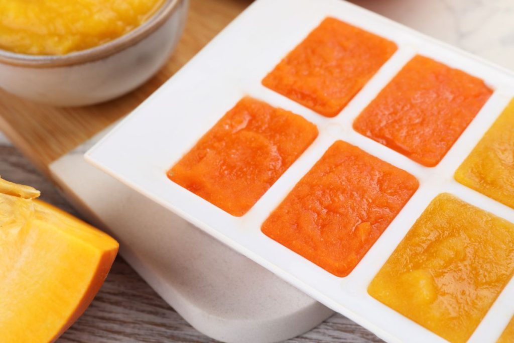 Pumpkin puree inside of ice cube molds with a cut pumpkin off to the side
