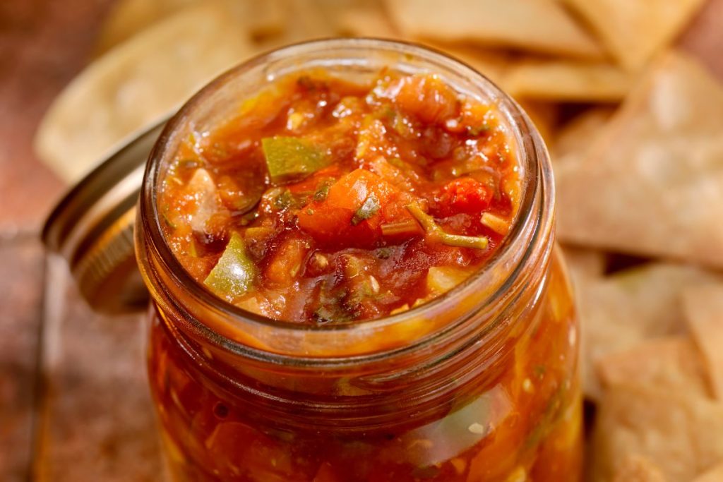 Canned jar of salsa that is open with tortilla chips in the background