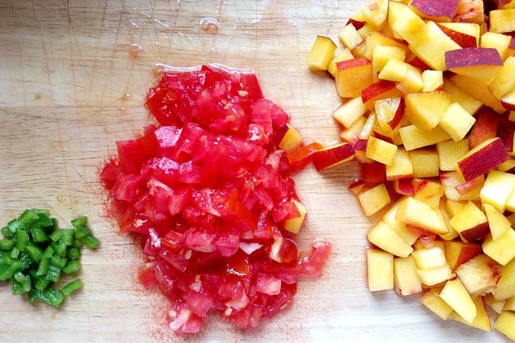 Diced jalapenos, red onions and peaches on a cutting board