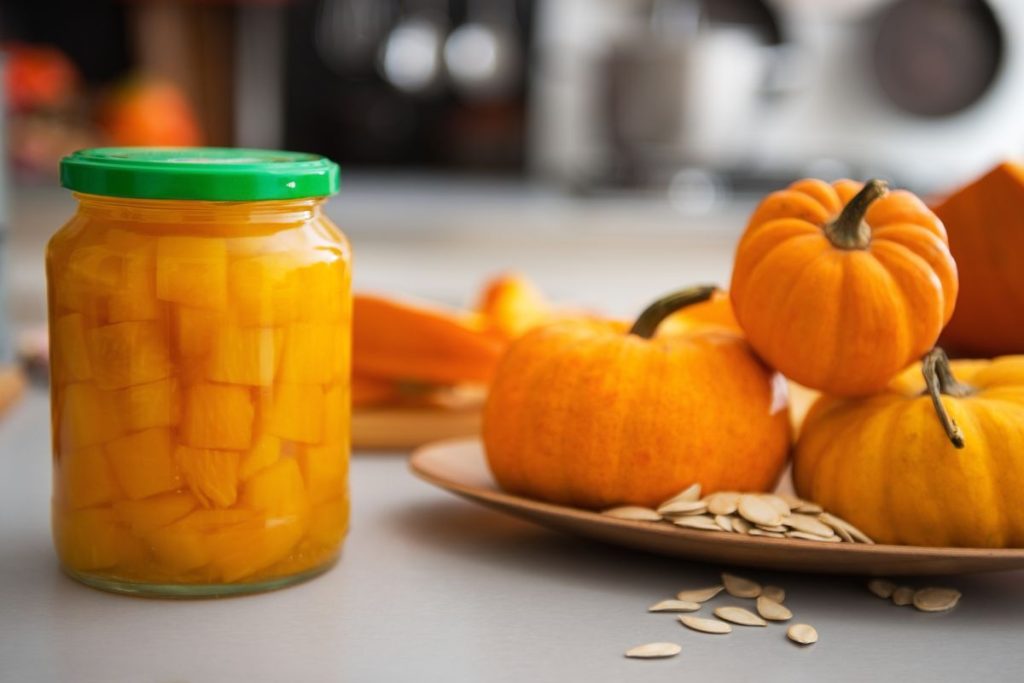 Jar of canned pumpkin next to stacks of pumpkins and pumpkin seeds