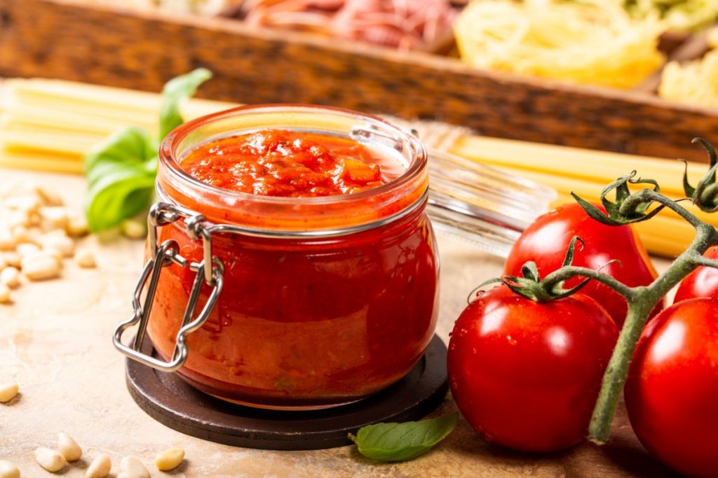 Jar of open pizza sauce next to tomatoes