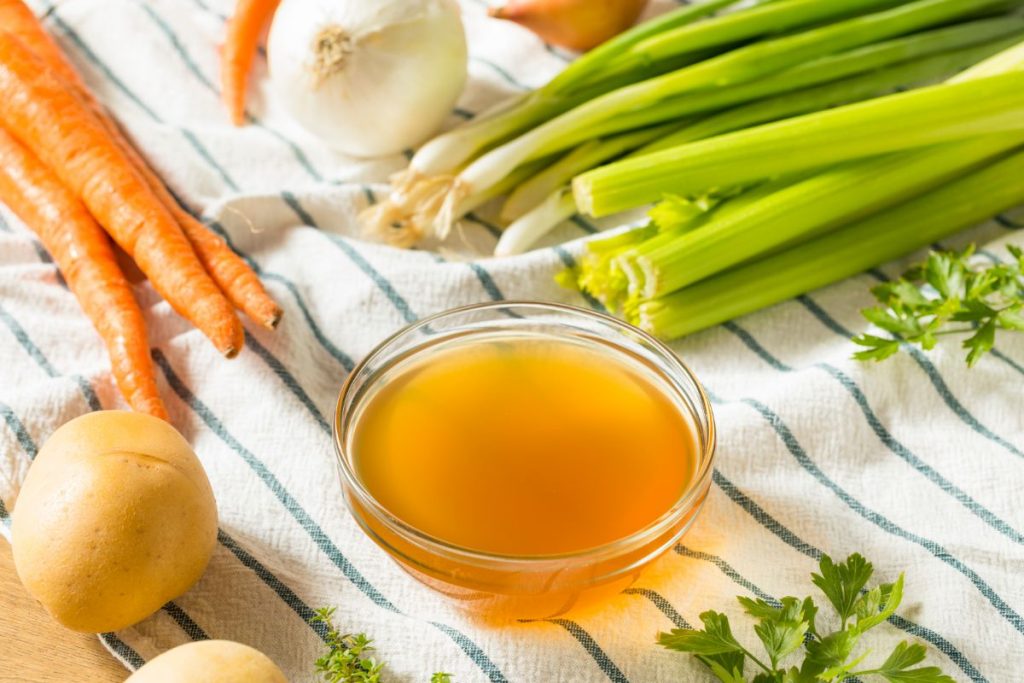 Bowl of vegetable stock surrounded by fresh vegetables