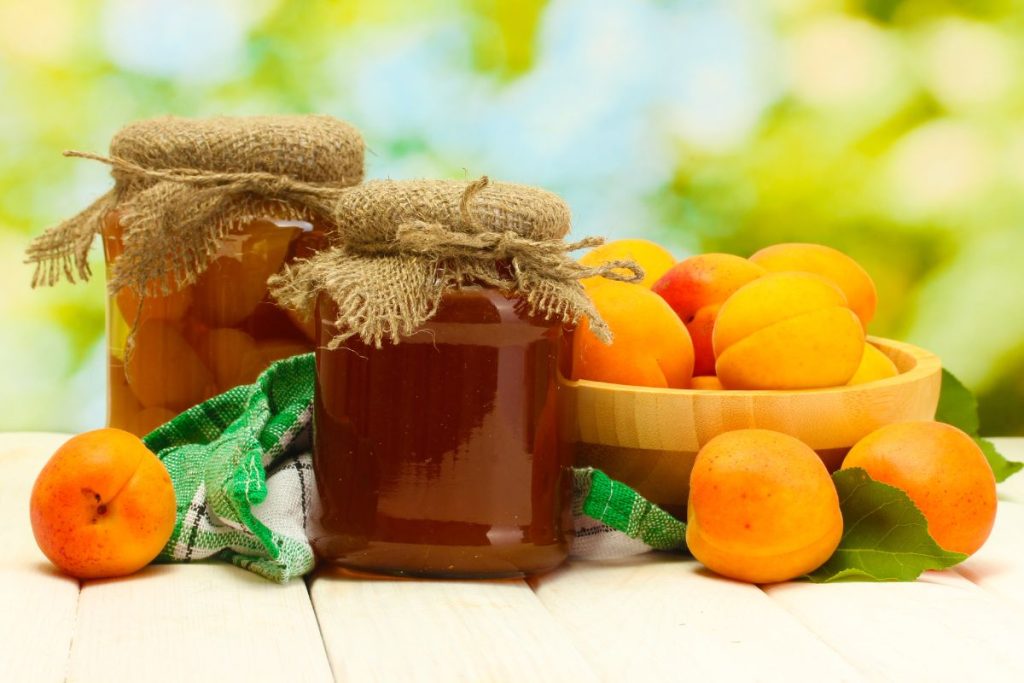 Jar of canned apricots and jar of apricot jam next to bowl of fresh apricots