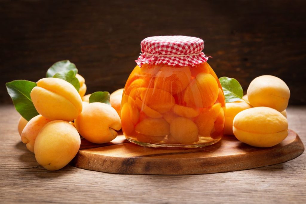Jar of canned apricots on cutting board with fresh apricots next to the jar