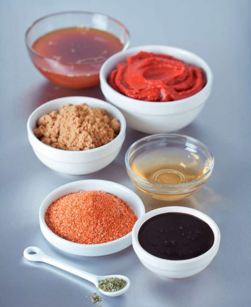 Bowls of bbq sauce ingredients including spices, honey, tomato paste and herbs