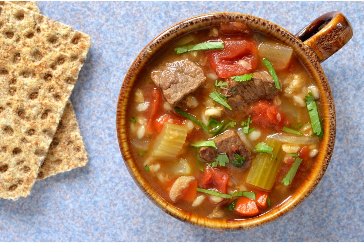 Beef and vegetable soup in a bowl with crackers