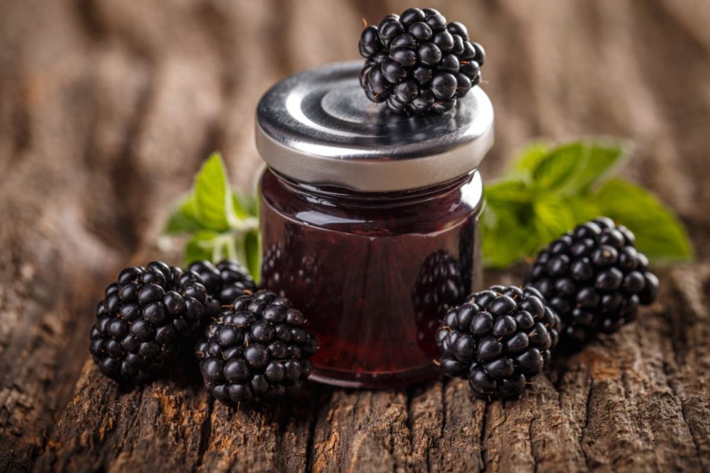 Small jar of blackberry jam surrounded by fresh blackberries