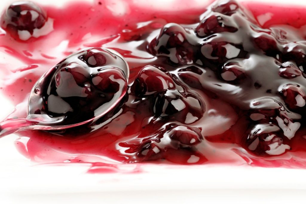 Blueberry pie filling on a plate with a spoon with large chunks of fruit and a thin, sauce like consistency