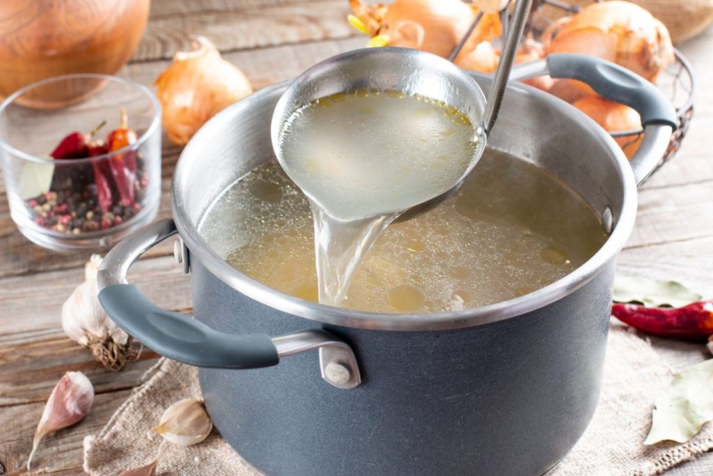 Pot full of chicken broth and a ladle inside the pot