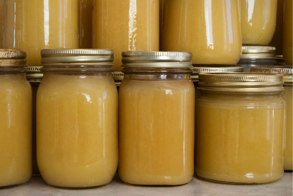 Jars of canned applesauce stored upright, and stacked on a table