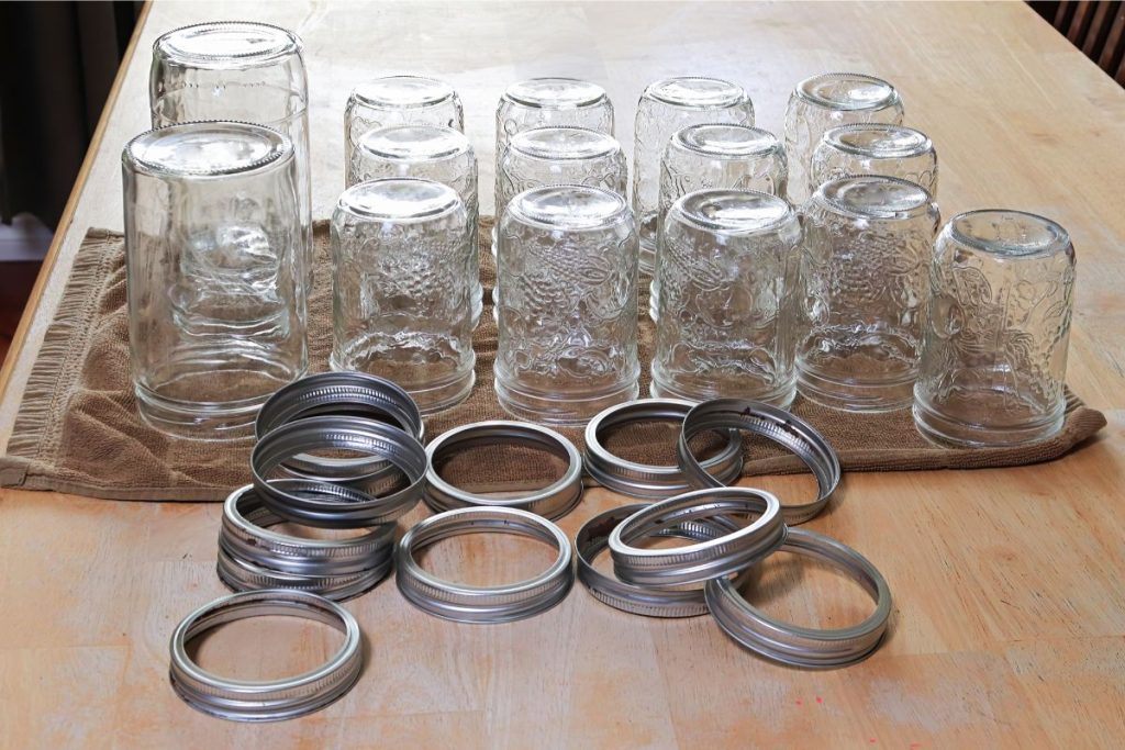 Empty canning jars standing upside down on a towel next to a pile of screw bands