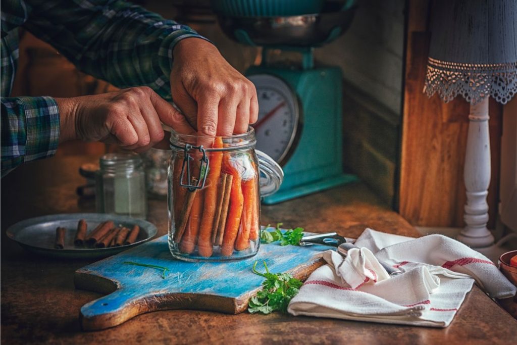 Raw packing carrots into canning jar with cinnamon sticks