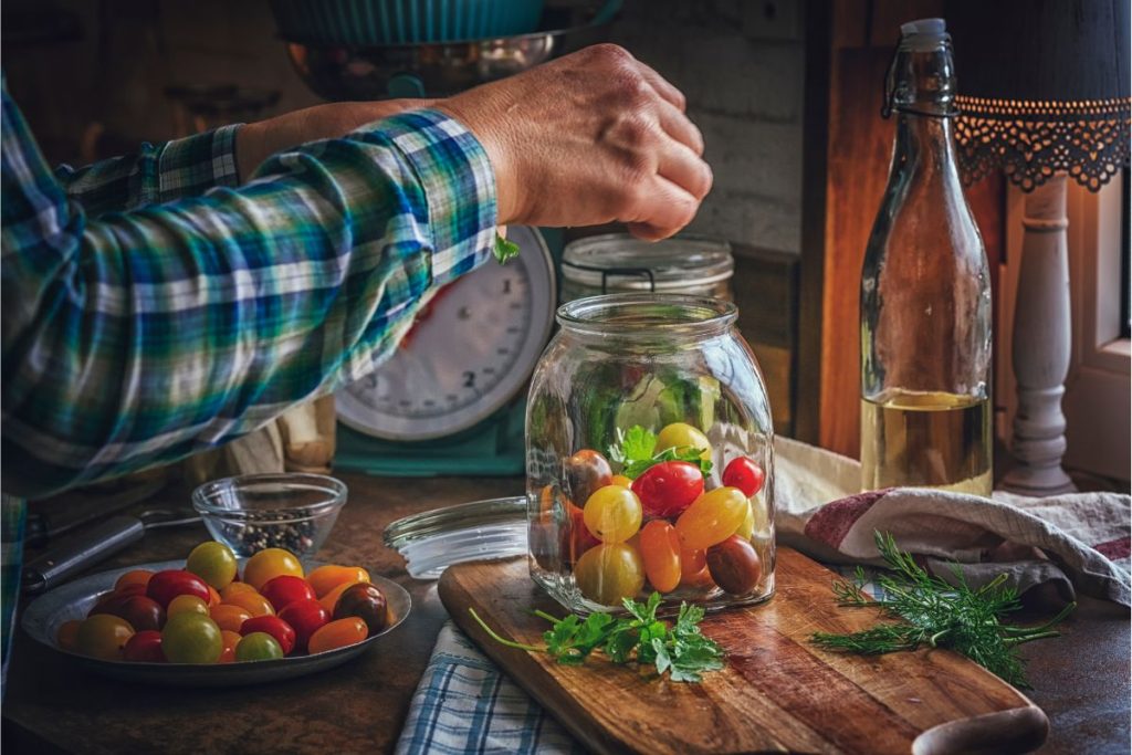 Man putting raw tomatoes and herbs in a canning jar