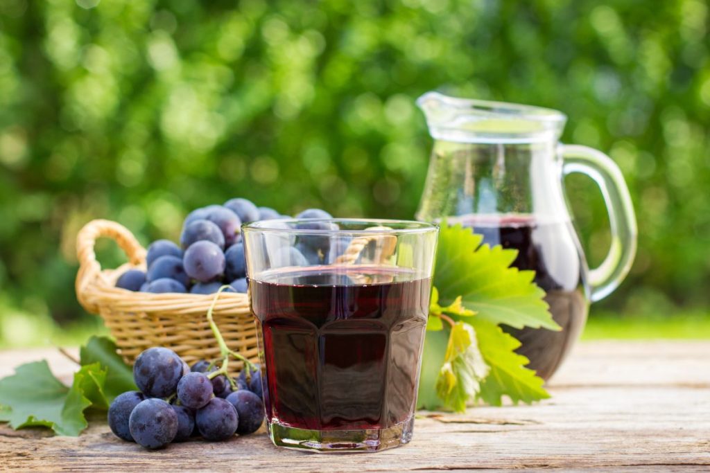 Grape juice in a glass on a table outside with fresh grapes and a pitcher of grape juice