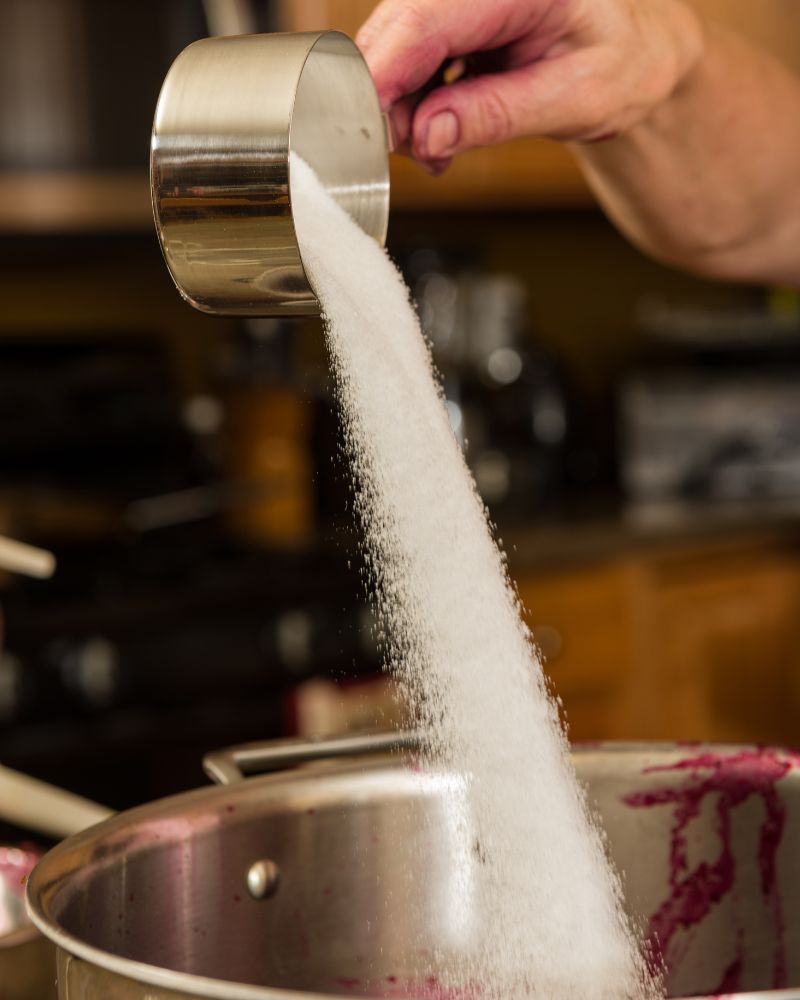 Pouring a half cup of sugar into a pot filled with grape juice